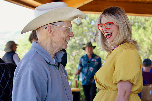 Older man with western hat smiling and talking with a Krysten Sinema look-a-like at a party event