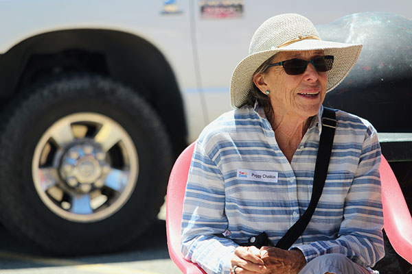 Woman in sunglasses and a hate sitting in a chair smiling and talking with others at a party event