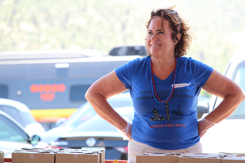 Woman wearing blue shirt with hands on her hips watching a speech